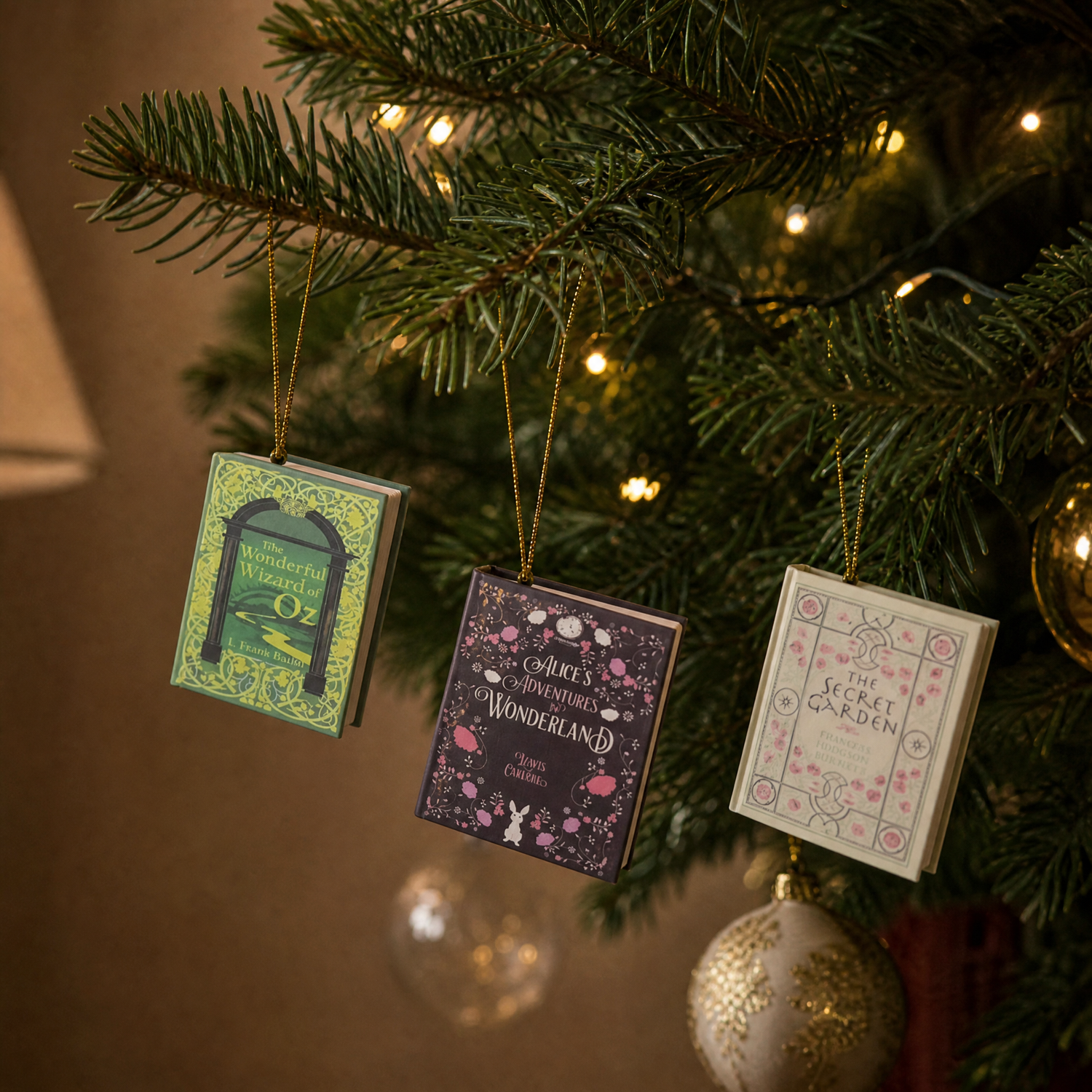 Three mini book ornaments hanging from a Christmas tree branch by gold cords